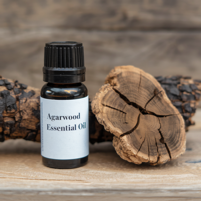 A photo of Agarwood Essential Oil bottle with a label. The label has the text Agarwood Essential Oil. There is a piece of Agarwood next to the bottle.